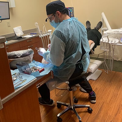 Dr. Neal Raval performing a dental surgery on his patient in the dental office, while wearing his blue business suit and operating instruments