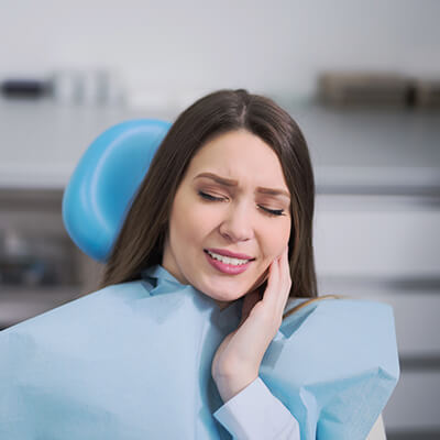 A young woman in the office with a toothache, while sitting in the dentist's chair, touching her cheek with her hands